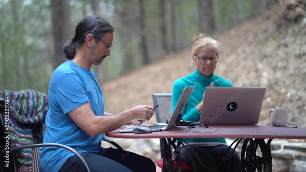 Mature man checks phone and a woman works on computer at a table outside. Mature man checks phone and a woman works on computer at a table outside.