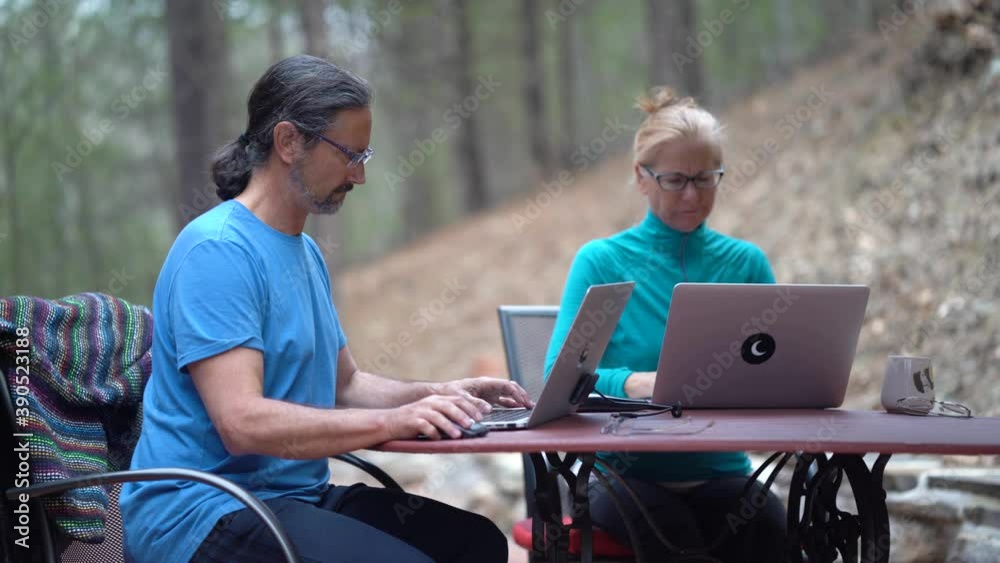 Mature man and woman work on computers at a table outside. Mature man and woman work on computers at a table outside.