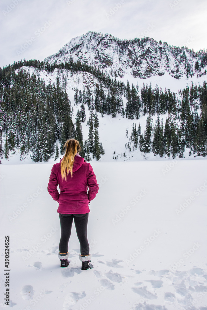 Winter sport activity. Adventurous woman standing on the shore of a snow covered lake, enjoying the beautiful view.