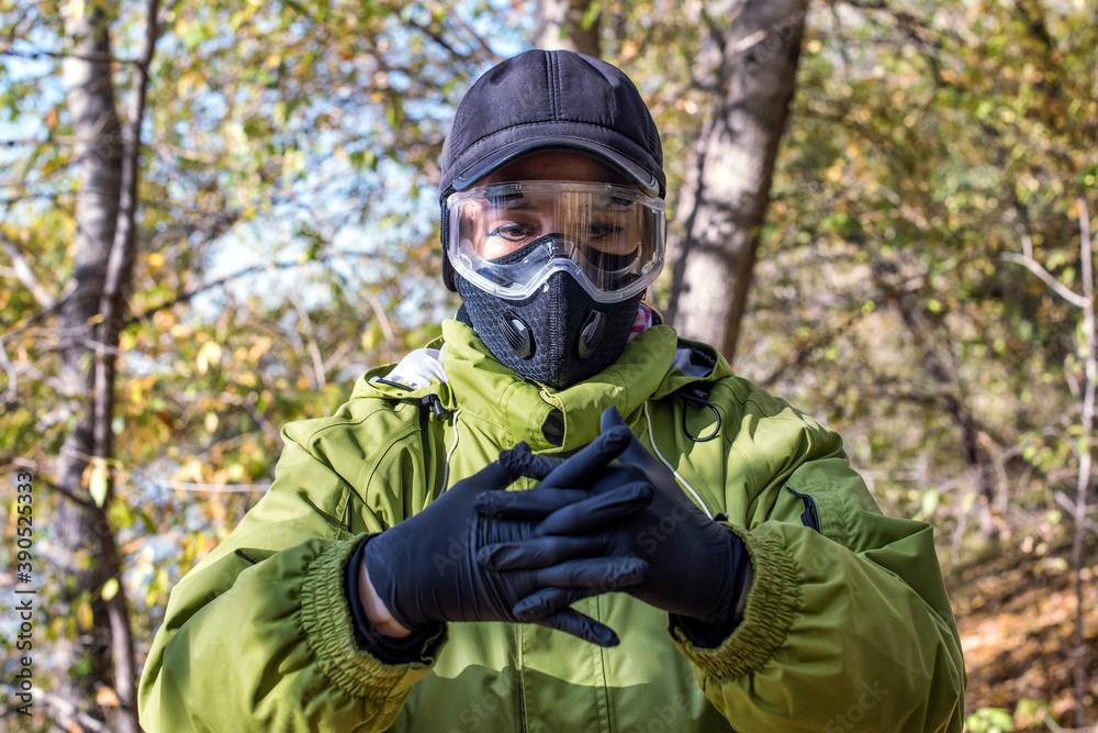 A woman wearing a respirator mask and protective glasses in the forest at COVID-19 period.