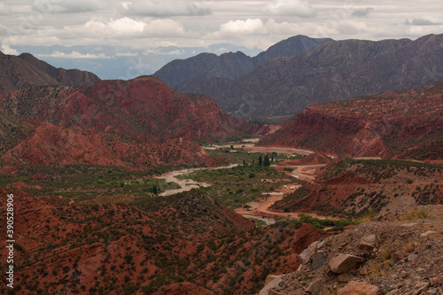 Geology. Panorama view of the red sandstone and rocky mountains, green forest and river flowing across the valley under a cloudy sky in Miranda Slope, La Rioja Argentina.