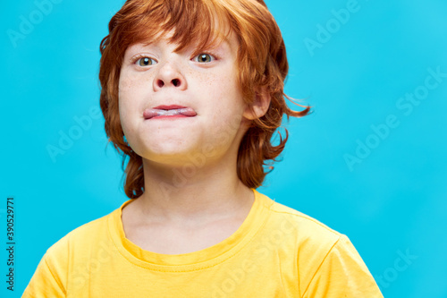 Close-up red-haired boy bites his tongue yellow t-shirt childhood fun 