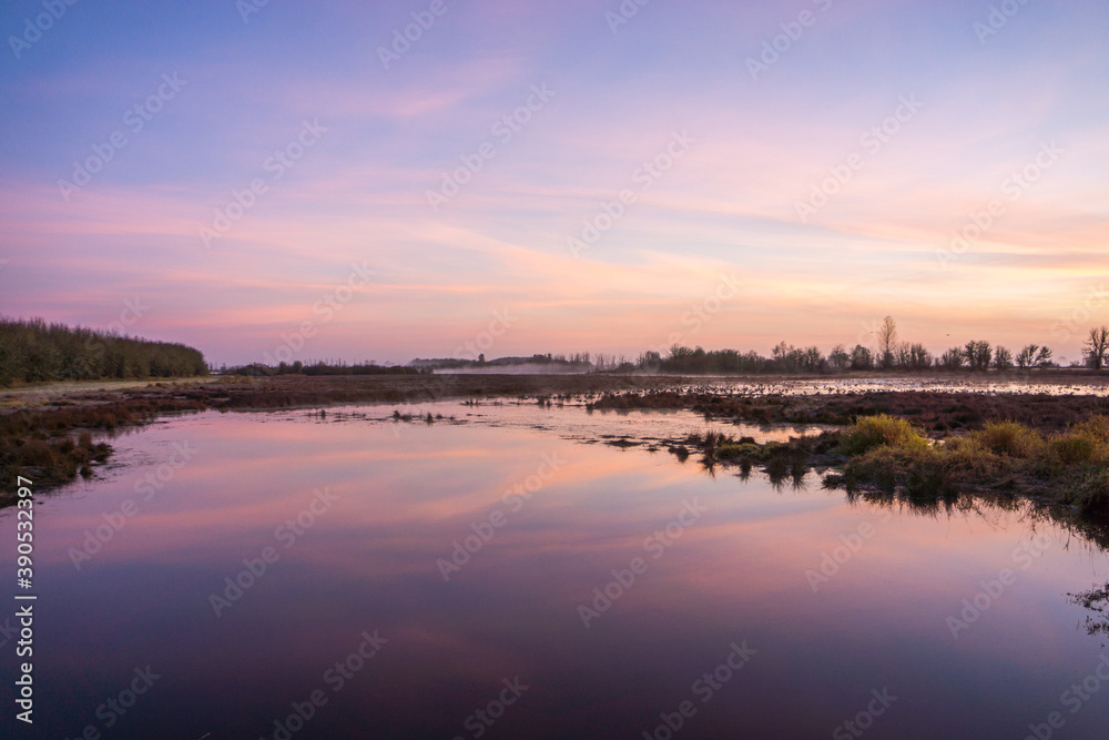 Early sunrise reflects subtle tones on the still surface of water in the foreground.