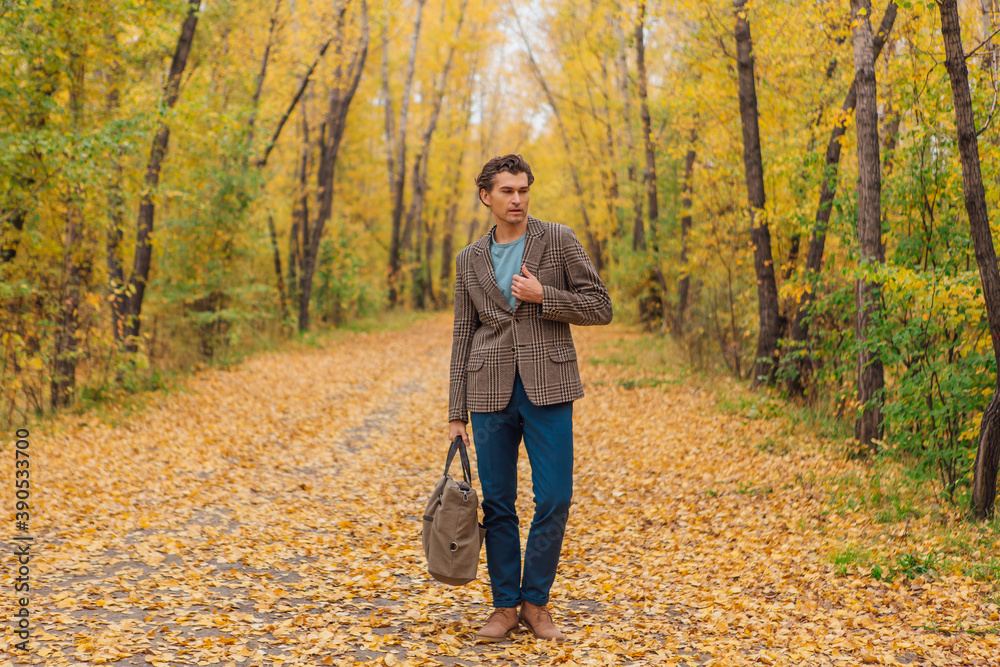 Tall handsome man with a bag on the autumn alley