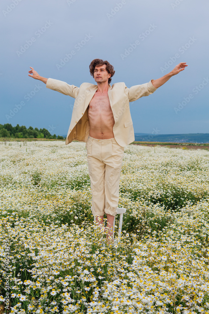 Tall handsome man dancing on the white chair in camomile flowers field Tall handsome man dancing on the white chair in camomile flowers field