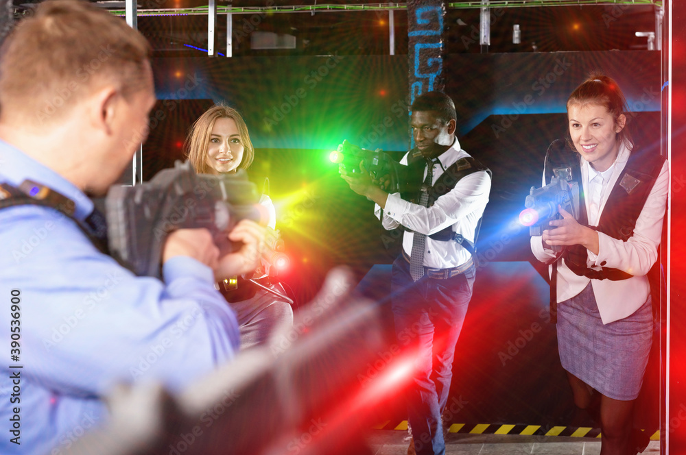 Glad cheerful men and women in business suits playing laser tag emotionally in dark room