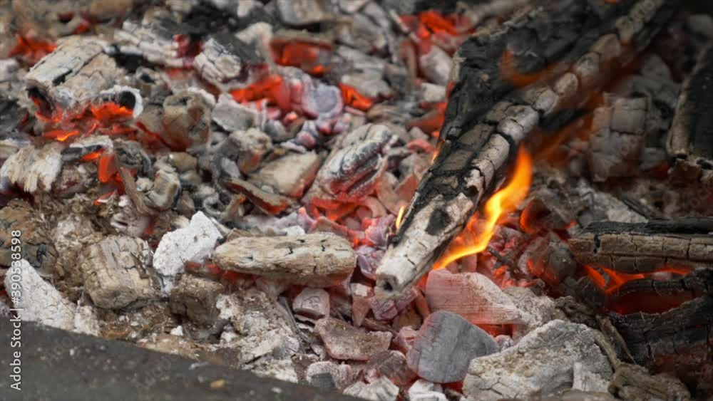 close up shot of hot charcoal on a barbecue plate and wood in flames on the right side close up shot of hot charcoal on a barbecue plate and wood in flames on the right side