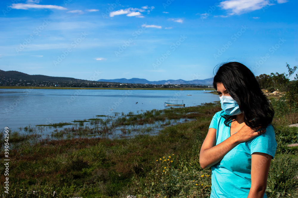 mujer joven con cubrebocas preocupada a la orilla de un lago