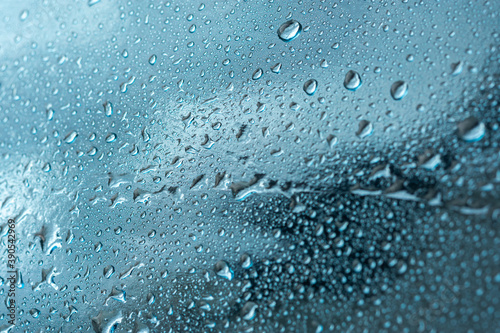 Abstract background with raindrops and beautiful blue bokeh. The concept of autumn and the cold stormy weather. Texture of macro drops on the blurred background of the window. Loneliness sadness