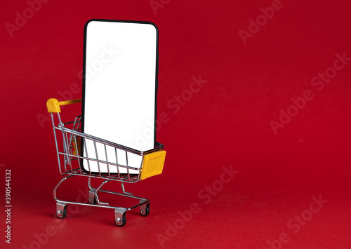 One single phone in the grocery cart on red background: online shopping, buying gifts for the New year or a gift for Valentine's Day! Side view, cut out space for text, place for text