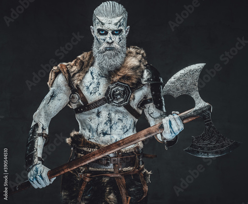 Risen night warrior in dark armour with fur and pale skn holding two handed axe in atmospheric dark background.