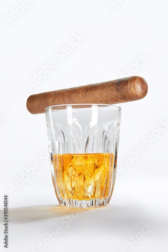 Closed up view of glass of whiskey with cigar on top on white back