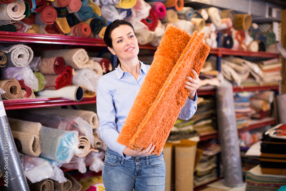 Adult woman buyer standing and choosing in shop with colour carpets