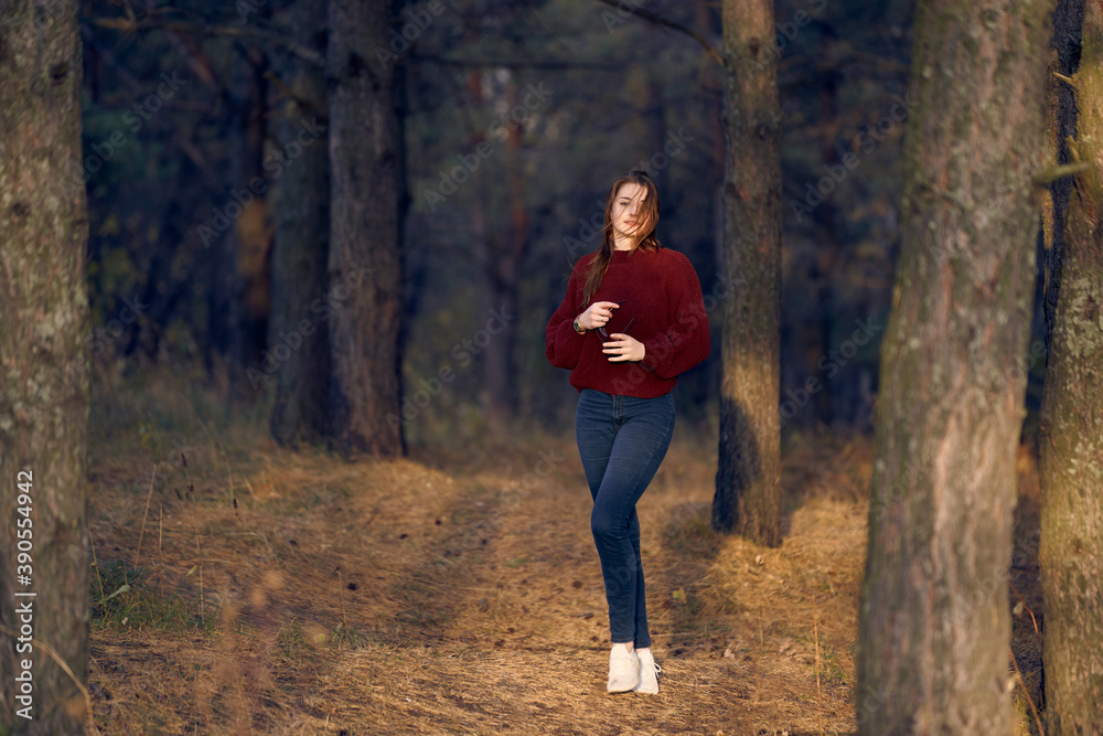 Lovely red-haired woman walks in nature. Autumn forest at sunset. Red sweater and jeans. Lovely red-haired woman walks in nature. Autumn forest at sunset. Red sweater and jeans.