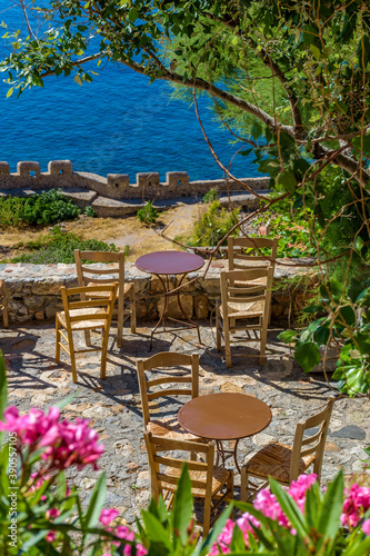 Fototapeta Naklejka Na Ścianę i Meble -  Traditional cafe exterior in the fortified medieval  castle of Monemvasia. Iron tables and wooden chairs with the view of the  aegean sea in the background.