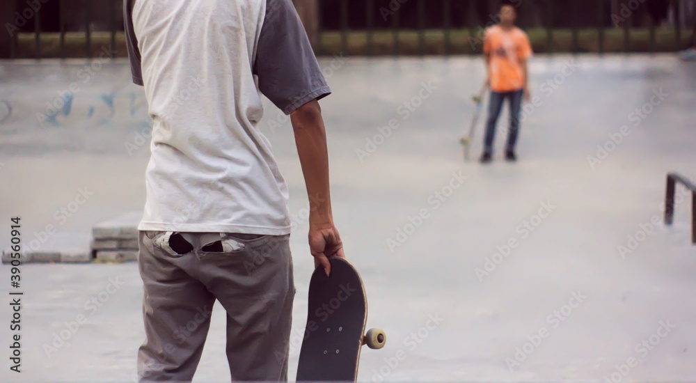 Obraz premium rear view of asian skateboarder with ripped pants playing on the skate park