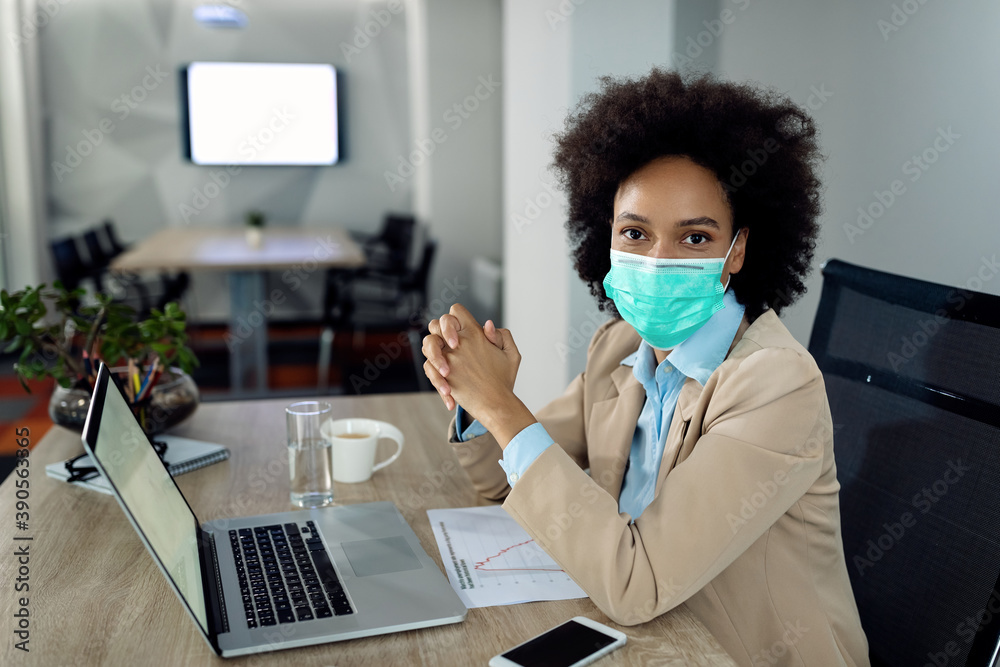 Black businesswoman with protective face mask working on laptop in the office. Black businesswoman with protective face mask working on laptop in the office.