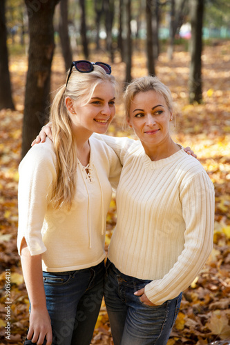 Mother and daughter in the park. Autumn and yellow leaves. Young mother and her toddler girl have fun.