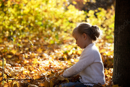 Girl sitting in the yellow leaves in the park.