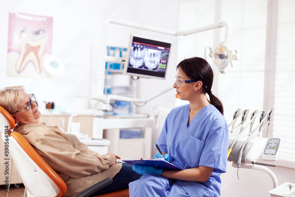 Dental assistant completing questioner during oral checkup of elderly patient. Senior woman talking with medical nurse in stomatology office about teeth problem. Dental assistant completing questioner during oral checkup of elderly patient. Senior woman talking with medical nurse in stomatology office about teeth problem.