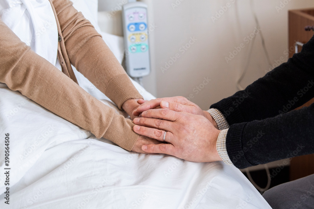 入院中の妻の手を握り元気付ける夫