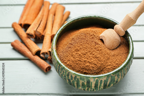 Bowl with cinnamon powder and sticks on wooden background