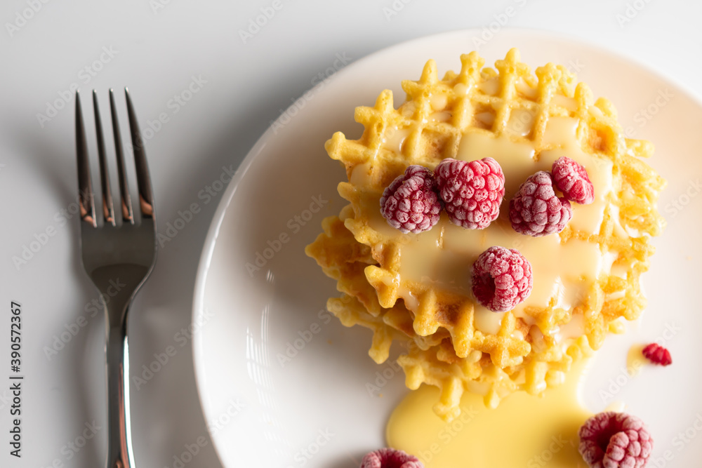 Weekend breakfast: waffles with condensed milk and raspberries. White background. Viennese waffles with condensed milk and raspberries on a white plate Weekend breakfast: waffles with condensed milk and raspberries. White background. Viennese waffles with condensed milk and raspberries on a white plate