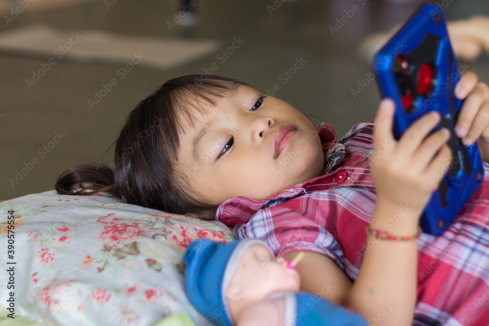 Obraz premium Selective focus. Portrait image of 2-3 years old baby. Happy Asian child girl using and playing a smart Phone. She laying on the bed.