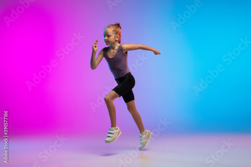 Healthy. Teenage girl, professional runner, jogger in action, motion isolated on gradient pink-blue background in neon light. Concept of sport, movement, energy and dynamic, healthy lifestyle.