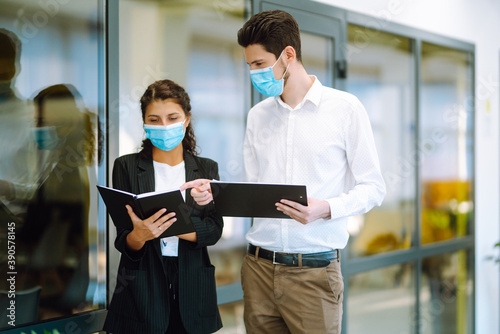 Two manager in protective face masks having an argument discussing business Issue. Holds a folder with important documents in his hands. Covid-19.