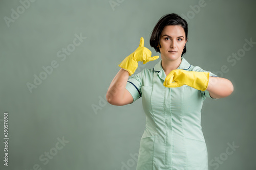 Young cleaning woman wearing a green shirt and yellow gloves showing it's time gesture © Cipri Suciu 