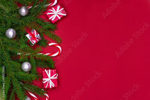 Christmas decorations layout or flatlay with fir branches  gifts  balls and candy canes on red background with copy space.