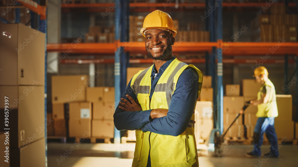 Handsome and Happy Professional Worker Wearing Safety Vest and Hard Hat Smiling with Crossed Arms on Camera. In the Background Big Warehouse with Shelves full of Delivery Goods. Medium Portrait Handsome and Happy Professional Worker Wearing Safety Vest and Hard Hat Smiling with Crossed Arms on Camera. In the Background Big Warehouse with Shelves full of Delivery Goods. Medium Portrait