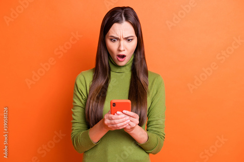 Photo of young beautiful shocked amazed surprised girl see bad comment in smartphone isolated on orange color background