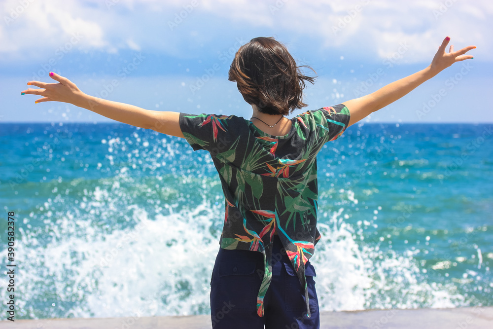 Happy girl with raised hands stands on the Mediterranean coast in Spain, sea vacations in Europe, no face visible. Happy girl with raised hands stands on the Mediterranean coast in Spain, sea vacations in Europe, no face visible.