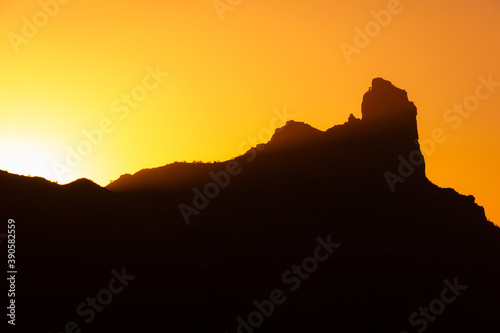 Splendid silhouette of Roque Nublo mountain with sun setting behind in Gran Canaria. Smooth sunrays on iconic natural landmark in Canary Islands, Spain. Enlightenment concept