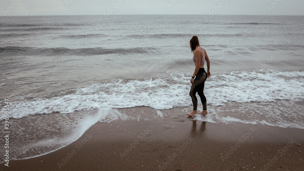 Young beautiful woman walking at the beach after working out wearing sporty clothes Young beautiful woman walking at the beach after working out wearing sporty clothes