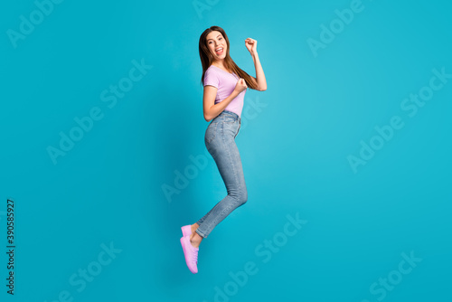 Full length photo of attractive cheerful student lady wear casual purple t-shirt jeans jumping high isolated blue color background