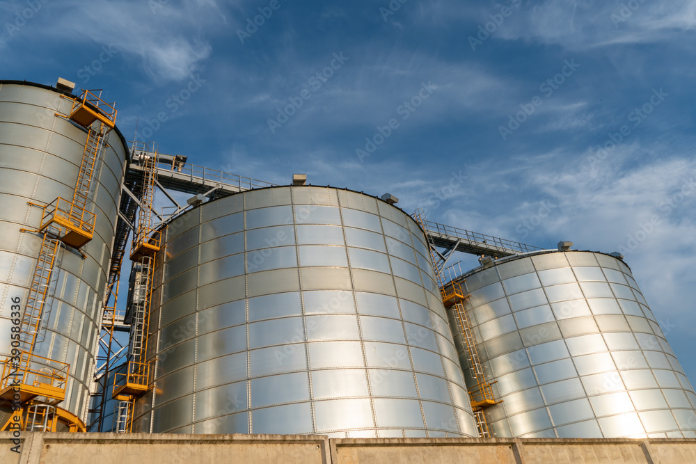 silver silos on agro manufacturing plant for processing drying cleaning and storage of agricultural products, flour, cereals and grain. Large iron barrels of grain. Granary elevator silver silos on agro manufacturing plant for processing drying cleaning and storage of agricultural products, flour, cereals and grain. Large iron barrels of grain. Granary elevator