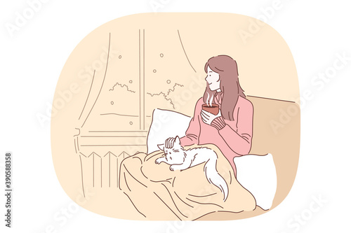 Comfort, rest, cozy relaxation with cat and hot tea in bed at home concept. Young smiling girl drinking tea or coffee in bed, petting cat and relaxing looking at window at home 