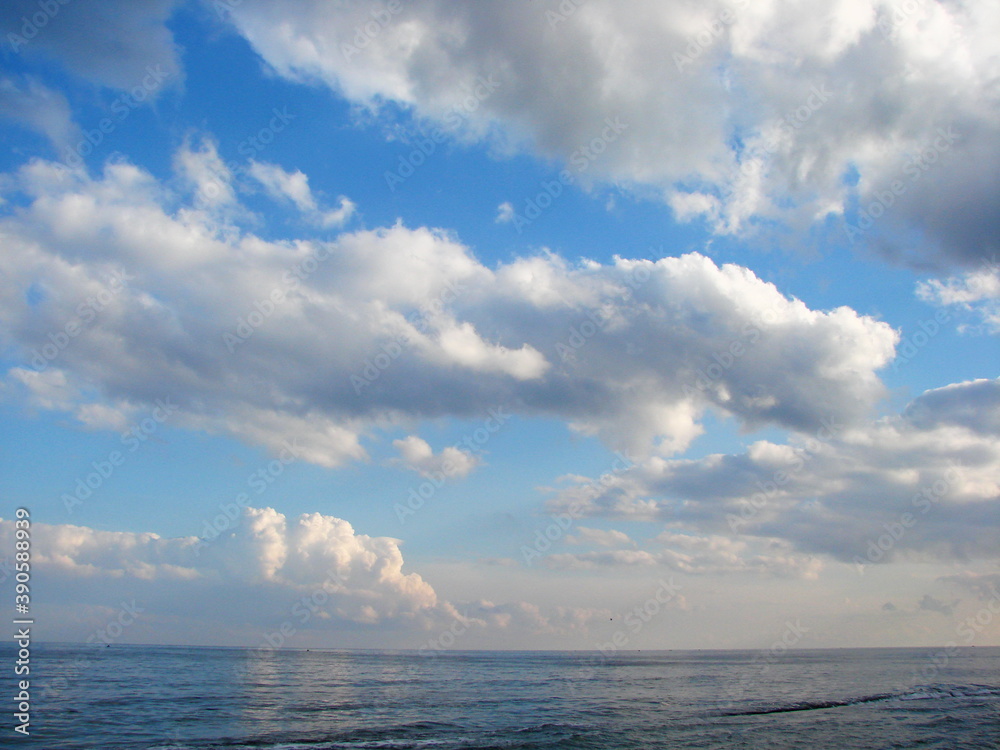 Bottom view of snow-white clouds illuminated by sunset in the blue sky over the surface of the sea.