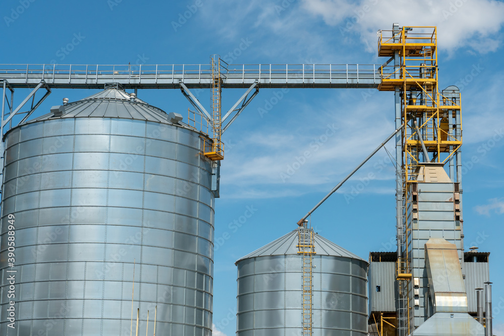 silver silos on agro manufacturing plant for processing drying cleaning and storage of agricultural products, flour, cereals and grain. Large iron barrels of grain. Granary elevator silver silos on agro manufacturing plant for processing drying cleaning and storage of agricultural products, flour, cereals and grain. Large iron barrels of grain. Granary elevator