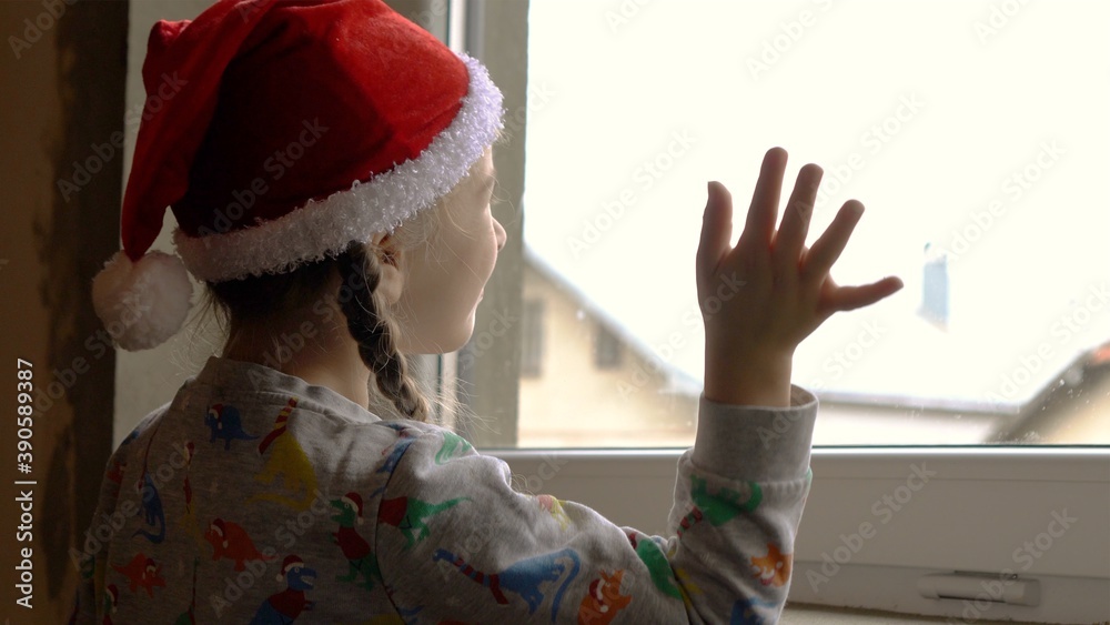 Little girl by the window in Santa hat. Orphans and Christmas . Orphanage life and holidays.