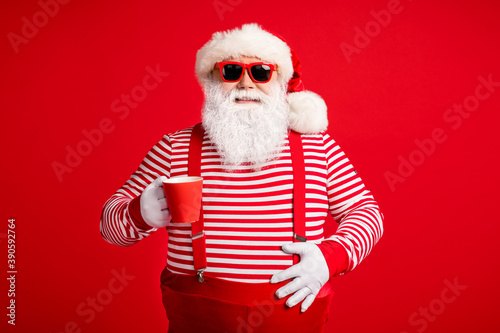 Portrait of his he nice handsome attractive cheerful Santa father drinking cacao eggnog festal day touching abdomen isolated bright vivid shine vibrant red color background © deagreez