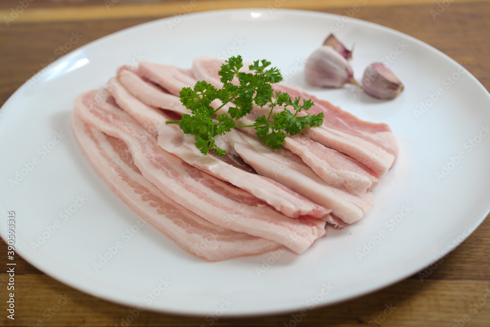 raw bacon with parsley on white plate raw bacon with parsley on white plate