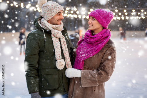 people and leisure concept - happy smiling couple talking at outdoor skating rink in winter over snow