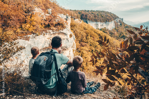 Father with two little boy traveling in the mountains. Hiking with children on a family trip. Traveling on vacation with a child, looking at the view. Active autumn rest