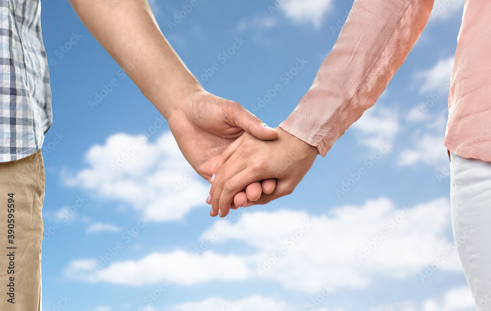 love, relationships and people concept - close up of happy couple holding hands over blue sky and clouds background