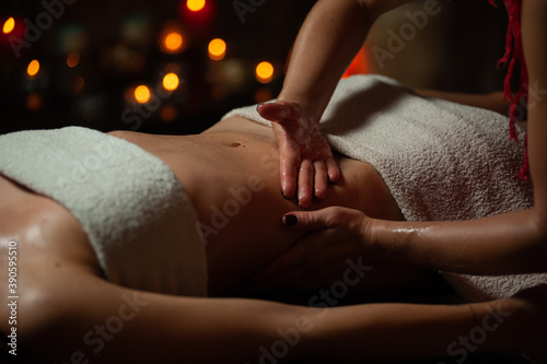 Close up of therapist doing stomach massage on woman in spa against dark background.