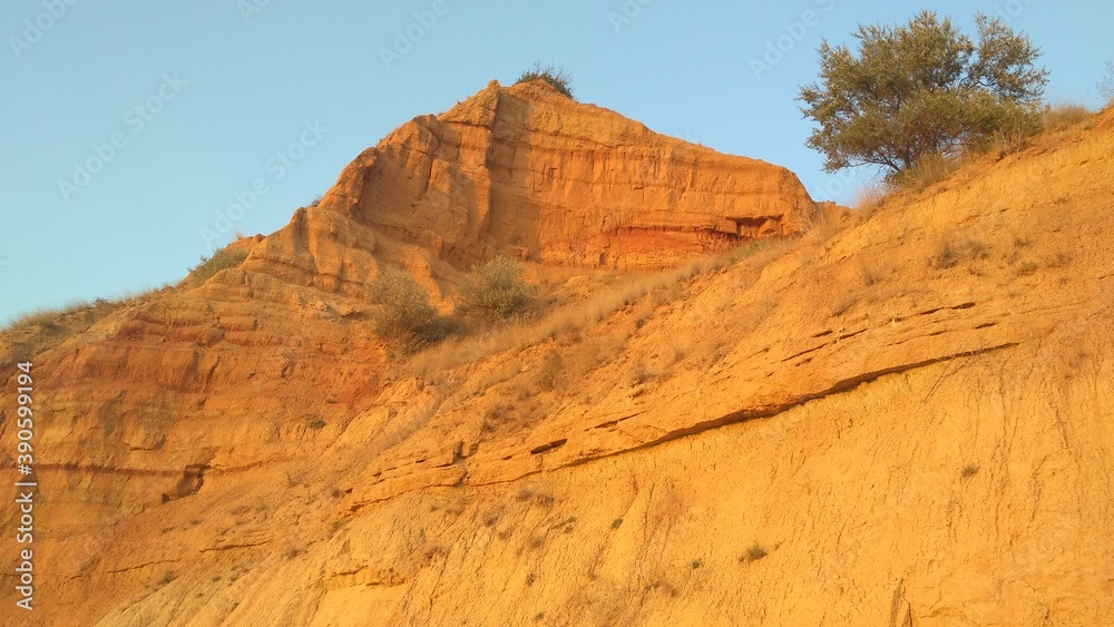 Red orange sandy precipitous rocks and cliffs. The section of the sand mountain shows the geological layers of ancient deposits. Nature creates beautiful landscapes. Evening amazing pre sunset sky.